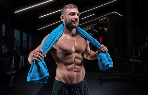 Muscular man posing in the gym with a towel on his shoulders. Fitness concept.