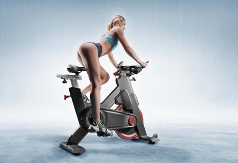 Beautiful slender and long-legged girl sits on an exercise bike. Side view. The concept of sports