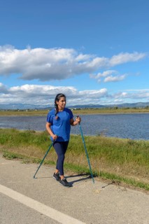 Outdoor enthusiast with walking poles beside a tranquil water body on a bright day