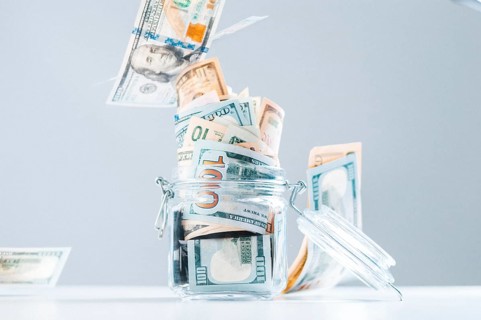 Glass piggy bank full of money. Banknotes are strewed from above. The concept of squandering.