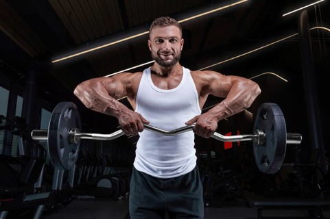 Handsome young man working out with a barbell in the gym. Shoulder pumping. Barbell pull to the chin. Fitness and bodybuilding concept
