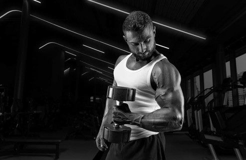 Muscular man in a white t-shirt works out in the gym with dumbbells. Biceps pumping. Fitness and bodybuilding concept.
