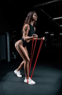 Tall athletic woman posing with gymnastic elastic bands in the gym. Fitness and bodybuilding concept.