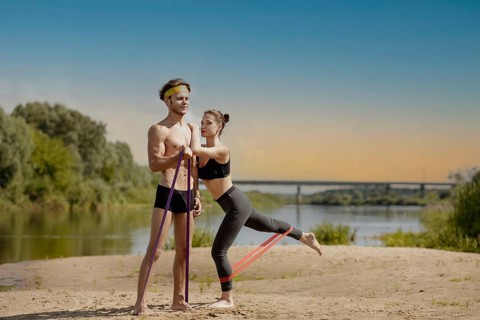 Young athletic couple doing exercise with resistance band on the shore of a lake on a sunny day