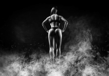 Image of a female athlete in a fire arena surrounded by smoke. Back view. Bodybuilding and fitness concept.