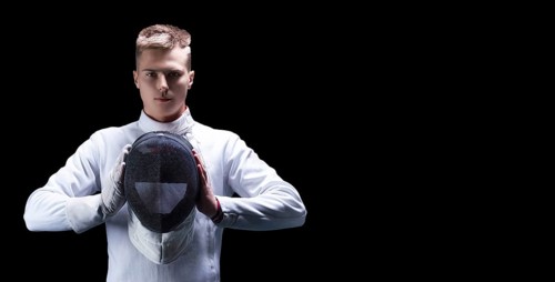 Portrait of a male fencer on a black background. He holds a helmet in front of him. The concept of fencing.