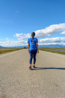 A traveler in casual attire treading along a paved road towards the horizon in a serene setting
