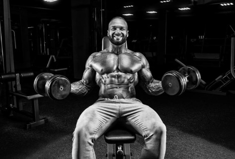 The athlete is doing the exercise in the gym. Lifting dumbbells while sitting on a bench. Fitness