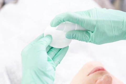 Image of hands in green gloves holding a spray bottle and cotton pads. Skin care concept.