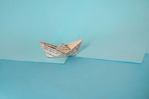 An origami paper boat on a two-tone background casting a long shadow