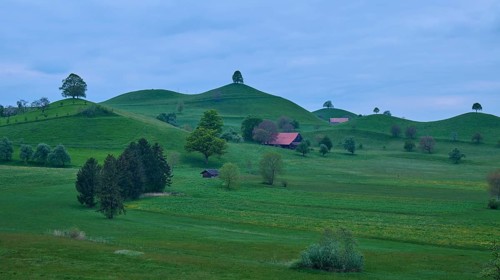 Green moraine hills landscape with meadows and lime trees and some small houses under a cloudy sky