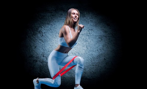 Charming girl does an exercise called lunges. Elastic band for training. The concept of fitness