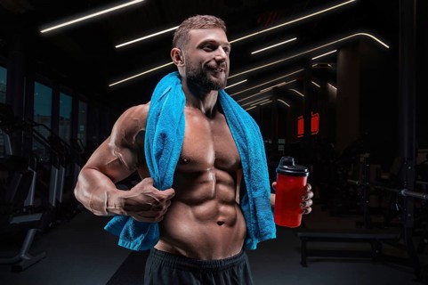 Portrait of a muscular guy with a naked torso and abs. Gym. Blue towel and red shaker. Fitness concept