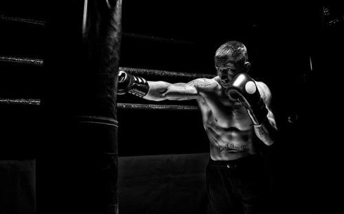 Professional boxer hits the bag against the background of the ring. Side view. The concept of sport and classic boxing.