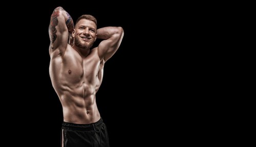 Young muscular guy with nice abs posing on a black background. Fitness and nutrition concept.