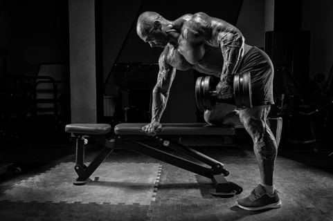 Muscular man pulls a dumbbell towards his stomach. Bodybuilding and powerlifting concept.