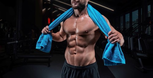 Muscular man posing in the gym with a towel on his shoulders. Fitness concept.