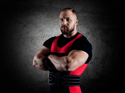 The weightlifter stands in a menacing pose with crossed huge arms and looks at the camera