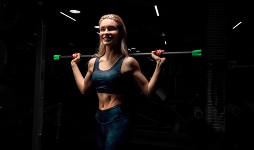 Charming blonde posing in the gym with a body-bar. Front view. The concept of sports