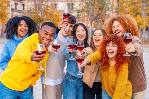 Multi-ethnic young people smiling and toasting with wine to the camera in the street