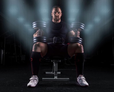 Professional weightlifter sits on a bench in the gym with two dumbbells on his lap