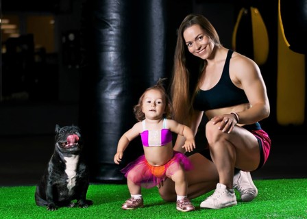 Charming sports mom trains in the gym with her little daughter and a French bulldog.