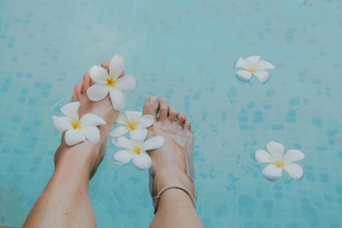 Feet adorned with plumeria flowers by a blue swimming pool