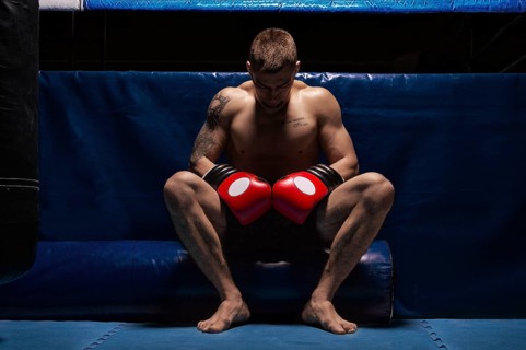 Boxer sits in gloves near the ring with his head bowed. The concept of sports