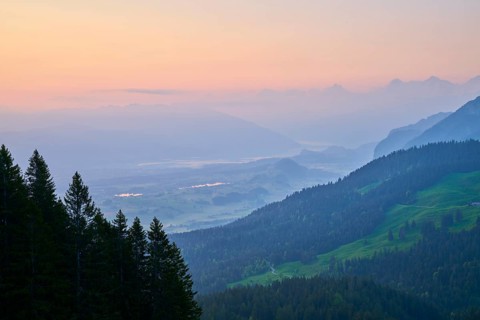 Sunrise over a misty mountain landscape with forest in the foreground