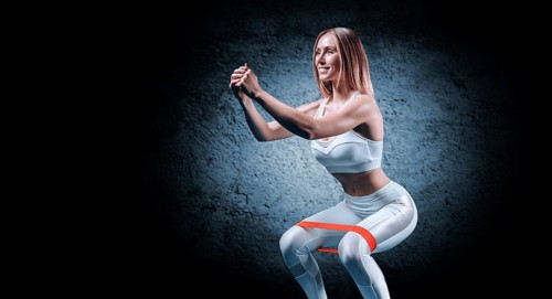 Charming girl is training in the gym with a rubber band. The concept of bodybuilding