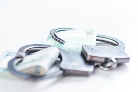 Packs of euros and hundred dollar bills are enclosed in handcuff bracelets. The concept of theft