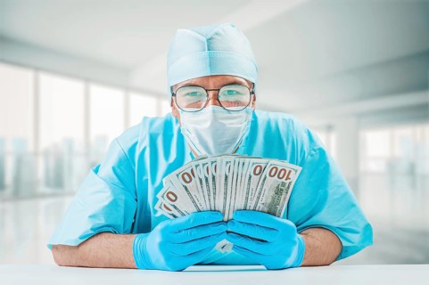 Portrait of a doctor holding hundred dollar bills. He is looking at the camera and smiling. The concept of corruption in medicine.
