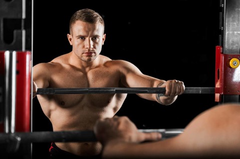 The weightlifter keeps his hands on the barbell and looks at himself in the mirror. Reflection in the Mirror