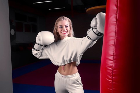 Cheerful and charming girl in a white sweatshirt boxing in huge gloves and smiling. The concept of sports