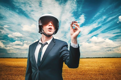 Portrait of a man in a helmet of a pilot. He stands in a field and launches a paper airplane. Business concept.