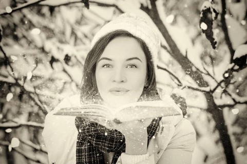 Charming woman blows bright dust from the pages of a book in the winter forest. Fairy tale concept. Christmas. New Year's holidays.