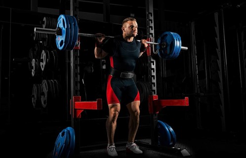 The weightlifter stands with a very heavy barbell on his shoulders. He is at the top and is preparing to sit down