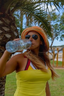 Happy woman drinking mineral water next to a palm tree enjoying the summer. Copyspace
