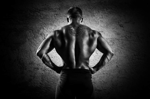 Huge weightlifter stands with his back to the camera and shows his huge back. Back view