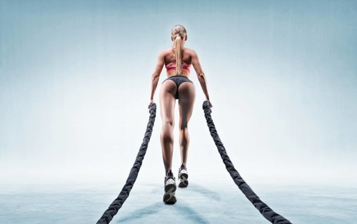 Sports girl trains with ropes. Back view. The concept of sports