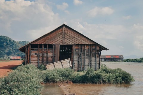 Derelict wooden shack on the riverbank surrounded by greenery. Kampot