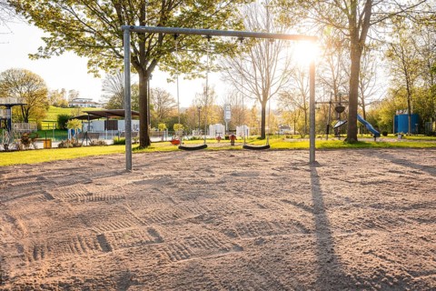 Swing set on sandy ground in the evening light with trees in the background