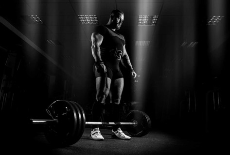 The weightlifter is preparing to perform an exercise called deadlift. He stands directly above the barbell and looks at it