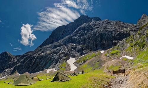 Tents of mountain hunters in the foreground with imposing mountain cliffs and blue sky with foehn clouds in the background