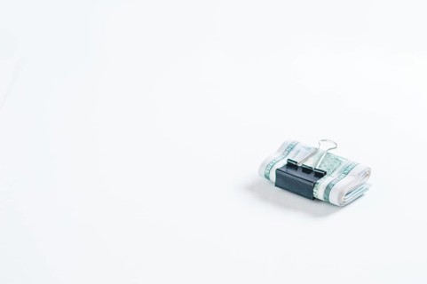 Pack of hundred-dollar bills lies on a white table fastened with a paperclip. The concept of savings during the crisis.