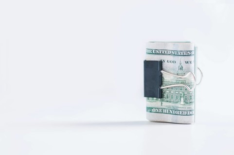 Pack of hundred-dollar bills lies on a white table fastened with a paperclip. The concept of savings during the crisis.