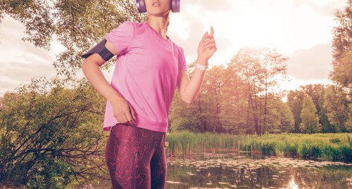Portrait of a beautiful girl running in a sunny park in headphones with a smartphone. Music apps concept.