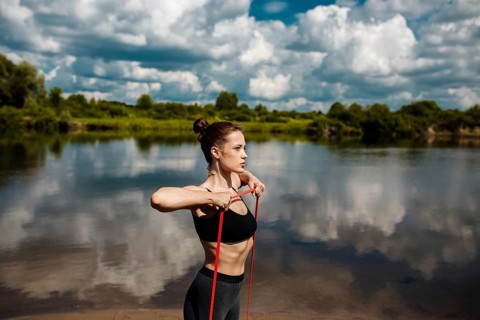 Athletic woman goes in for sports in nature in summer on the beach with resistance band