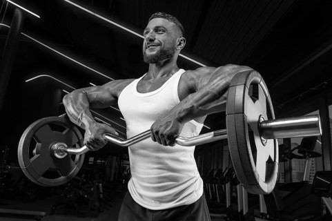 Handsome young man working out with a barbell in the gym. Shoulder pumping. Barbell pull to the chin. Fitness and bodybuilding concept