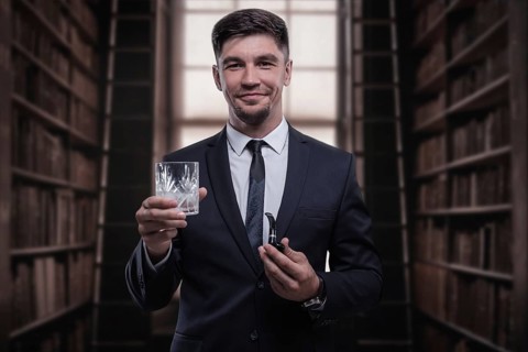 Portrait of an elegant man in a suit with a smoking pipe and a glass in the library. Business concept.